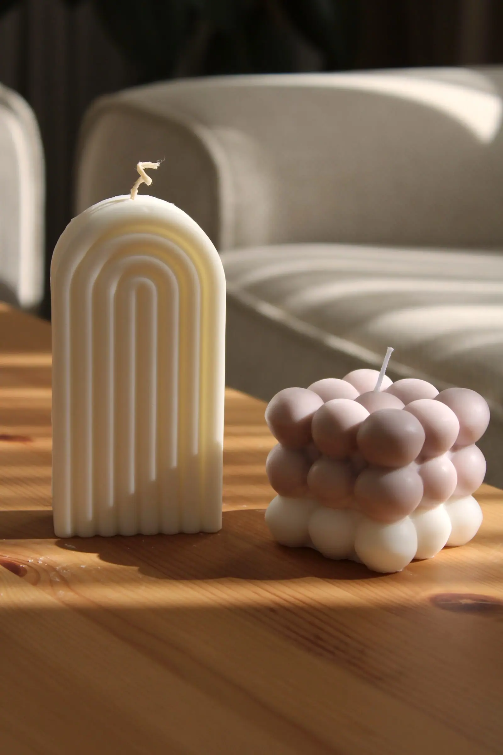 Modern candles with unique designs placed on a wooden table in a cozy room.